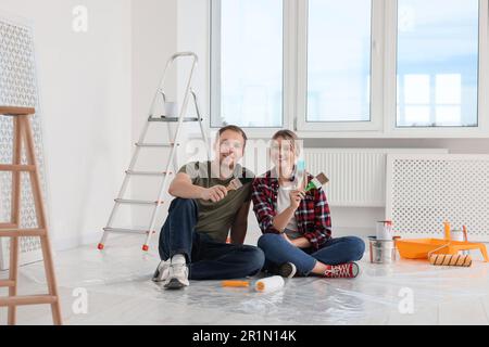 Couple heureux avec des brosses et des outils de peinture sur le sol dans l'appartement pendant la réparation Banque D'Images