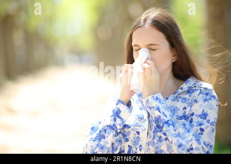 Femme allergique soufflant sur des tissus marchant en été dans un parc Banque D'Images