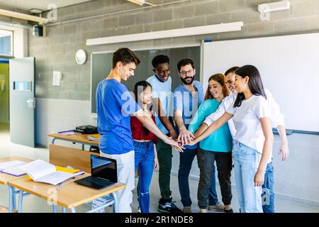 Un jeune groupe de camarades de classe étudiant empilant les mains avec l'enseignant en classe Banque D'Images