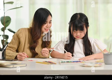 Mère asiatique de soutien aidant l'enfant avec l'affectation scolaire, l'écriture et le dessin avec le crayon dans le carnet à la table Banque D'Images