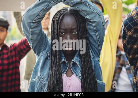 Détails sur une jeune femme noire marchant lors d'une manifestation. Elle a un perçage de nez et de longues dreadlocks. Elle a ses poings élevés et croisés au wis Banque D'Images