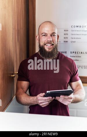 Il y a toujours de la place pour la technologie dans votre entreprise. Portrait d'un beau jeune barbier utilisant une tablette numérique tout en travaillant à l'intérieur de son barbershop. Banque D'Images