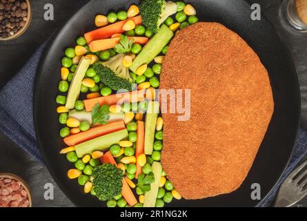 Schnitzel de poulet frit servi avec de délicieux légumes sautés sur fond de bois sombre. Banque D'Images