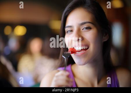 Bonne femme mangeant de la fraise dans un restaurant et regarde l'appareil photo Banque D'Images