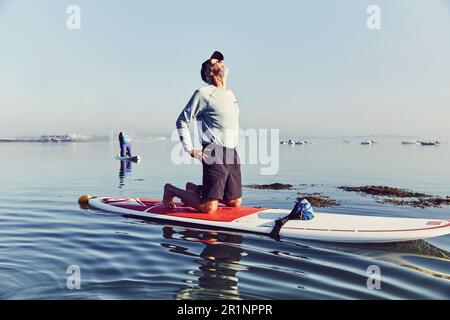 Une paddle boarder de stand-up se balance dans une posture de yoga au lever du soleil dans le brouillard Banque D'Images