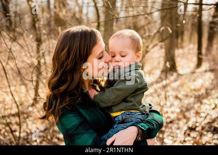 La mère souriante apporte le visage près de la joue de bébé dans les bois en automne Banque D'Images