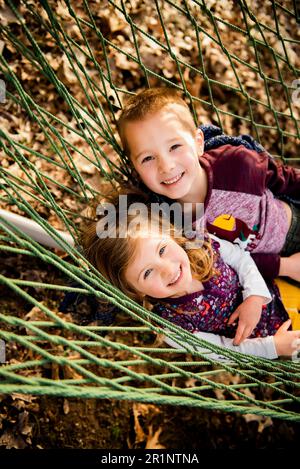 Frère souriant et sœur se détendre dans un hamac en automne regardant la caméra Banque D'Images
