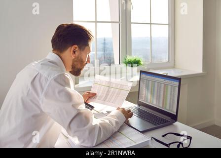 Vue latérale d'un jeune homme d'affaires comptable travaillant avec un ordinateur portable avec des tables au bureau et dactylographie. Banque D'Images