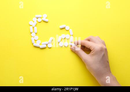 Femme faisant le symbole de calcium avec des pilules blanches sur fond jaune, vue de dessus Banque D'Images