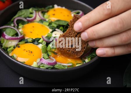 Femme trempant un morceau de pain dans le jaune d'œuf, gros plan. Manger un Shakshuka savoureux Banque D'Images