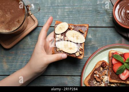 Femme portant de savoureux toasts avec de la pâte à tartiner au chocolat, des noix et de la banane à une table en bois, vue du dessus Banque D'Images