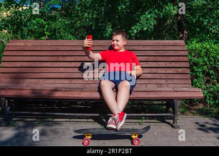 Garçon assis sur le banc et communique par chat vidéo à l'aide d'un smartphone et d'Internet. Banque D'Images