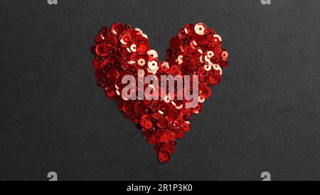Paillettes rouges en forme de coeur sur fond noir, plat Banque D'Images