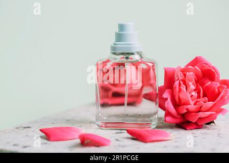 Bouteille de parfum en verre et fleurs roses corail sur table en pierre naturelle, gros plan. Banque D'Images