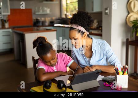 Une mère afro-américaine souriante aide sa fille à faire ses études en utilisant une tablette à la maison Banque D'Images