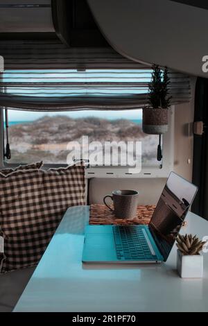 Image verticale de la nomade numérique intelligente liberté de travail alternative bureau vanlife style de vie concept. Un ordinateur portable sur la table de la dinette d'une fourgonnette. Vacances modernes et travail d'affaires Banque D'Images