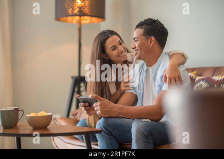 Couple amoureux reposant sur un canapé confortable, amusant, applications pour smartphone, profiter de la vidéo à distance, garçon montrant site Web intéressant à la petite amie, choisir des biens de services en ligne e-commerce concept Banque D'Images