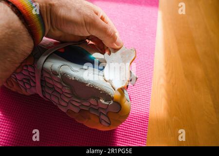 Un homme inspecte une chaussure de course déchirée, sa semelle est décollée et endommagée. Il le tient dans sa main pour évaluer les réparations nécessaires pour les chaussures d'équipement de sport de luxe. Banque D'Images