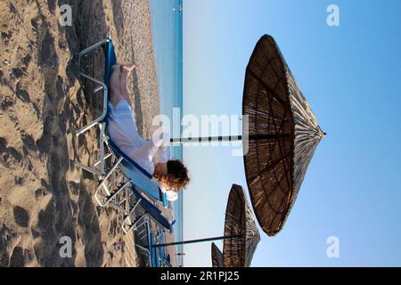 Jeune femme Grèce, île de Rhodes, Kiotari, plage de galets, parasol, Chaises longues, pédalo, Dodécanèse, île méditerranéenne Banque D'Images