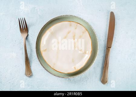 Une plaque vide avec un rebord doré, avec de l'argenterie, un plan de pose à plat. Vaisselle moderne Banque D'Images