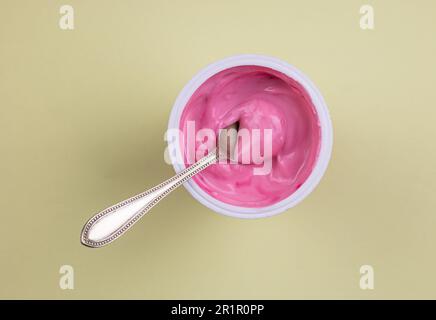 Yaourt rose rouge saveur velours dans une tasse en plastique isolé sur fond jaune pastel avec espace de copie Banque D'Images