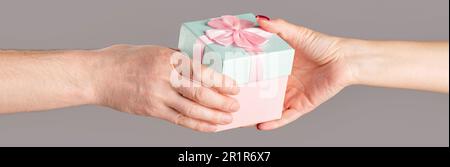 Homme mains tenant cadeau de Saint Valentin. Mains de sexe masculin et féminin tenant une boîte cadeau rose. Fille donne un cadeau à l'homme. Femme mains tenant cadeau Banque D'Images