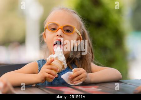 une petite fille heureuse avec le syndrome de down mange de la crème glacée en été sur une promenade Banque D'Images