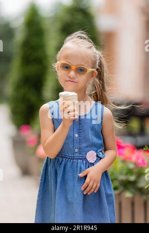 une petite fille heureuse avec le syndrome de down mange de la crème glacée en été sur une promenade Banque D'Images