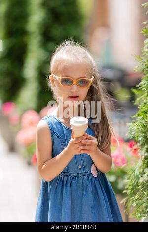 une petite fille heureuse avec le syndrome de down mange de la crème glacée en été sur une promenade Banque D'Images