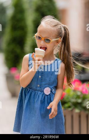 une petite fille heureuse avec le syndrome de down mange de la crème glacée en été sur une promenade Banque D'Images