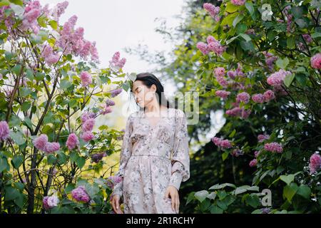 Une jeune femme brune se promène dans le jardin et aime les arbustes lilas en fleurs. Banque D'Images