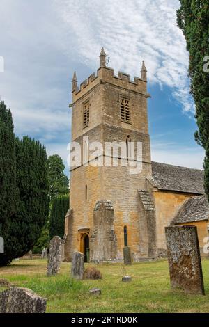 Stanway, Royaume-Uni-août 2022 ; vue à angle bas de la tour de l'église Saint-Pierre avec en face des pierres de tête altérées sur les tombes entre les arbres verts Banque D'Images