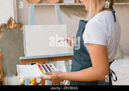 Gros plan d'une femme debout sur un chevalet avec maquette de papier vierge avec peintures aquarelle. Banque D'Images