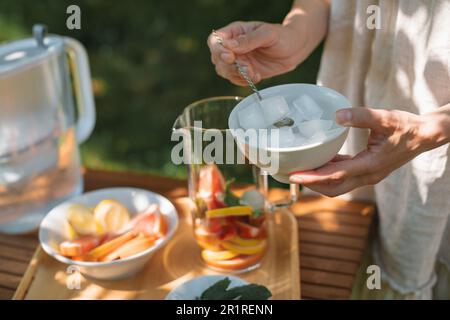 Femme préparant une carafe d'eau infusée avec des fruits frais et des feuilles de menthe dans le jardin Banque D'Images