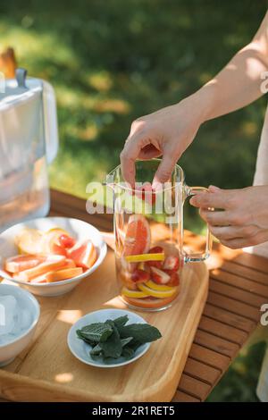 Femme préparant une carafe d'eau infusée avec des fruits frais et des feuilles de menthe dans le jardin Banque D'Images