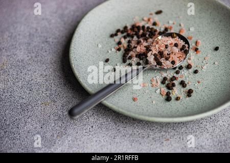 Gros plan d'une cuillerée de grains de poivre et de sel de romarin et de citron rose de l'Himalaya sur une assiette Banque D'Images