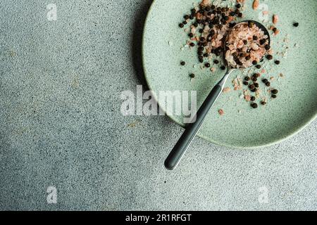 Gros plan d'une cuillerée de grains de poivre et de sel de romarin et de citron rose de l'Himalaya sur une assiette Banque D'Images