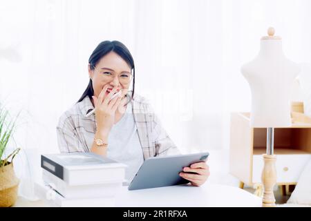 Femme souriante de mode assis à une table travaillant sur une tablette numérique Banque D'Images