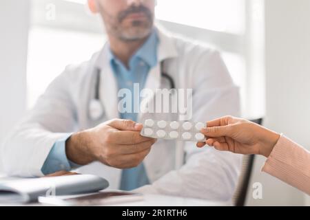 Médecin de sexe masculin consultant la patiente au sujet des pilules, prescrivant des médicaments, assis au bureau dans le bureau de la clinique, à proximité Banque D'Images