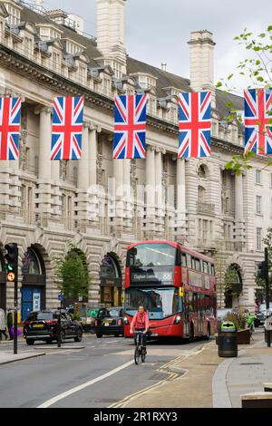 Londres, Royaume-Uni - 9 mai 2023; cycliste et bus rouge de Londres sur Regent Street avec drapeaux suspendus Union Jack Banque D'Images