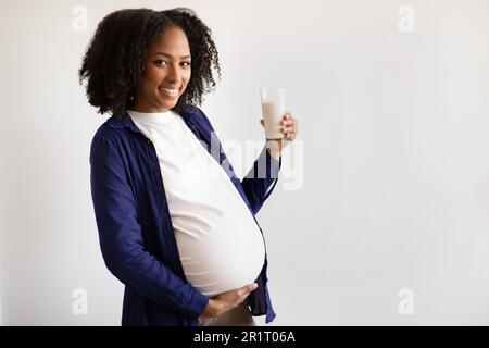 Joyeuse femme enceinte afro-américaine millénaire avec un grand ventre tenir un verre de lait sur fond de mur gris Banque D'Images