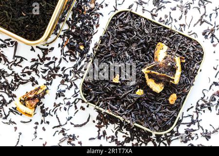 plat lay gros plan sur le thé noir à feuilles d'orange sec dans la boîte de la boîte et renversé sur la table blanche Banque D'Images