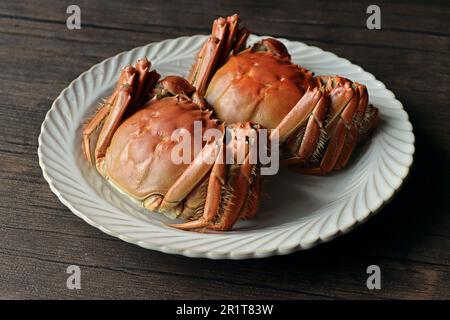 Deux grands crabes fraîchement cuits sur une assiette blanche au-dessus d'une table texturée en bois, prêts à être dégustés Banque D'Images