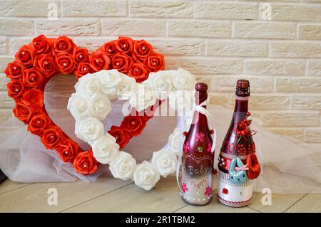 Coeur rouge et blanc avec roses. Deux bouteilles de champagne maison. Sur le fond d'un mur de briques. Banque D'Images