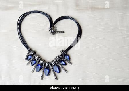 Cœur à la Saint-Valentin avec un magnifique collier féminin et tendance sur une bande en caoutchouc noir avec des pierres brillantes bleues, des diamants contre un tissu beige Banque D'Images