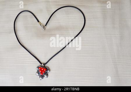 Collier pour femmes avec pendentif en argent et cercles rouges sous forme de coeur jusqu'au jour de Saint-Jean Saint-Valentin en fil noir sur fond beige. Banque D'Images