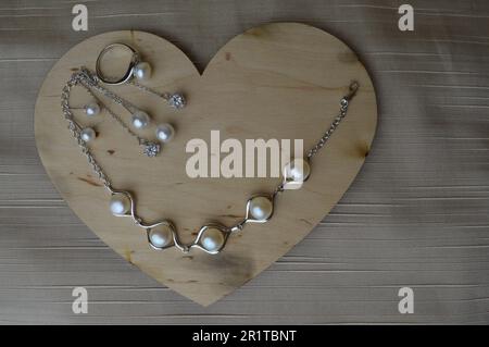 Un coeur en bois pour la Saint-Valentin avec ornements en argent, boucles d'oreilles, bagues, colliers avec perles, diamants, pierres précieuses, strass sur une ba beige Banque D'Images