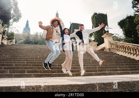 Groupe d'amis heureux multiraciaux ayant le plaisir de sauter dans la rue en écartant les bras. Trois adolescents multiculturels bondissant et riant ensemble. Des personnes diverses qui se traînaient avec joie. Photo de haute qualité Banque D'Images