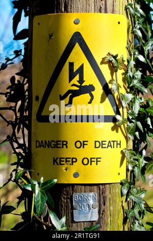 Gros plan d'un panneau jaune attaché au poteau en bois d'une ligne de transport d'électricité rurale avertissant d'électrocution et de danger de mort. Banque D'Images