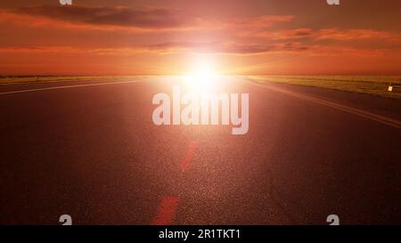 Longue route d'asphalte vide vers le soleil couchant Banque D'Images
